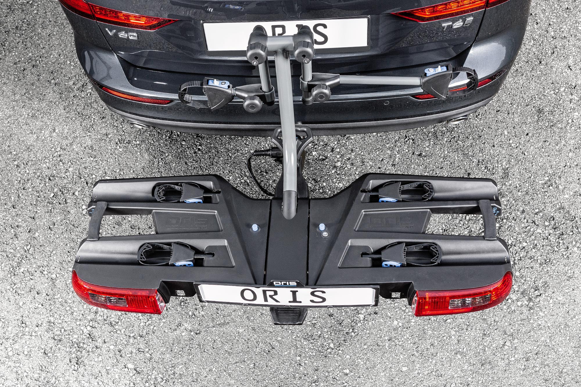 Top view of the ORIS TRACC FIX4BIKE bicycle carrier mounted on a dark grey Volkswagen Passat Variant, showing wheel trays, frame holders and integrated rear lights.
