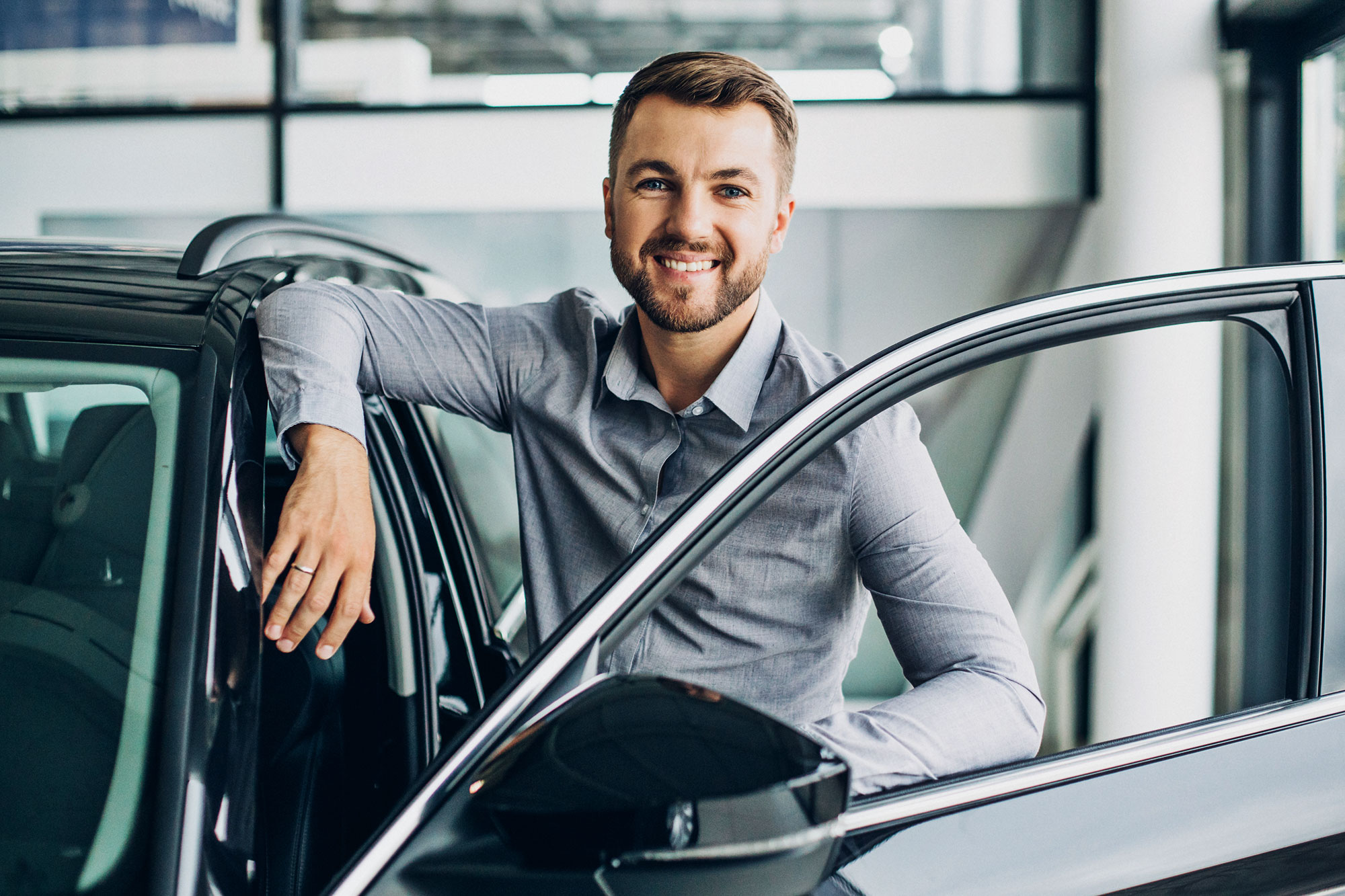 Smiling driver beside an open car door in a showroom after installation of an ORIS towbar.
