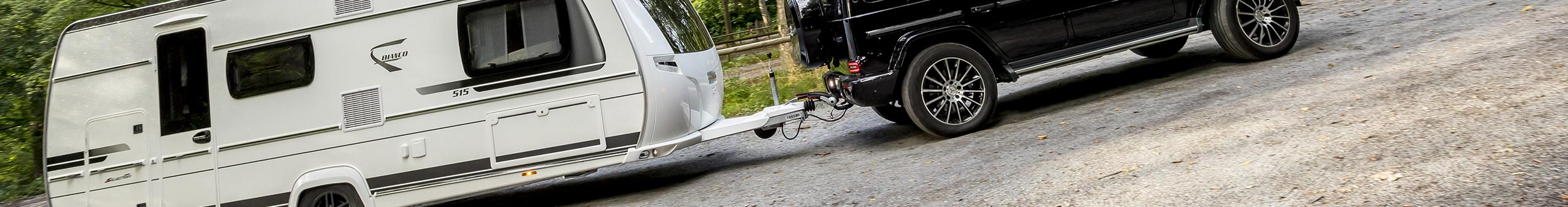 Mercedes-Benz G-Class towing a caravan with an ORIS towbar on a forest campsite road.