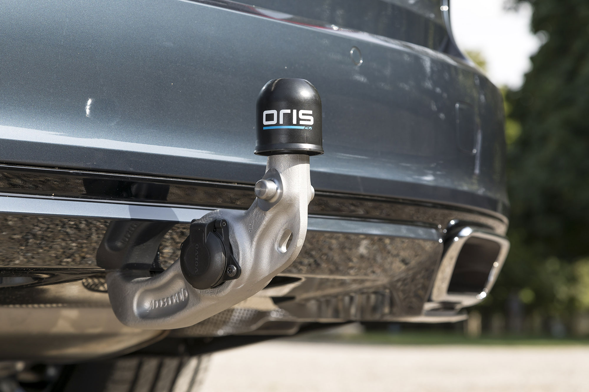 ORIS OEM fully electric swivelling towbar with protective cap and integrated electrical socket, factory-installed on a premium vehicle, shown in close-up from the rear.