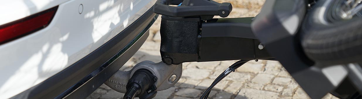 Close-up of ORIS TRACC bicycle carrier mounted on a towbar with FIX4BIKE connection system attached to a white Volvo estate car.