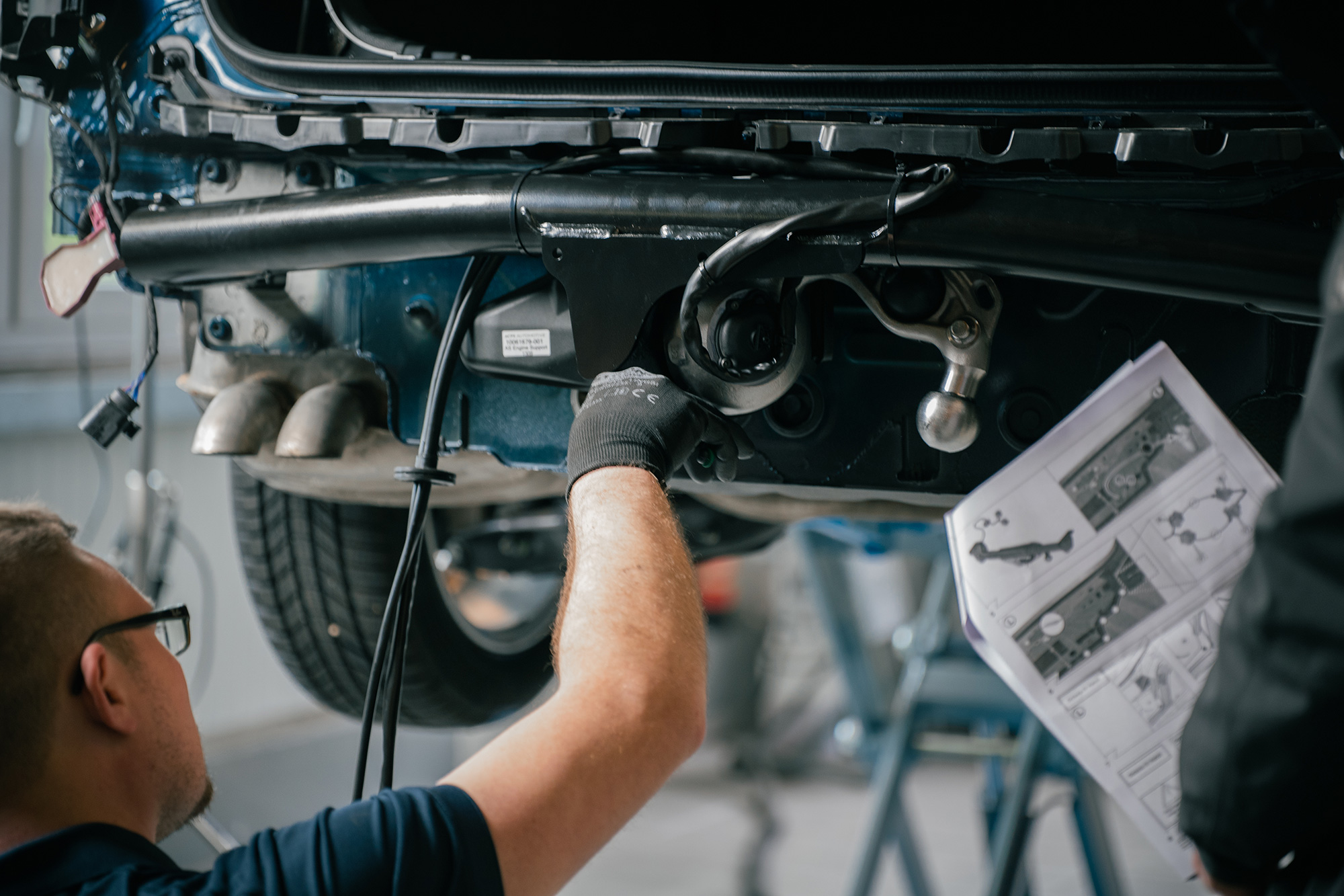 DUO complete set installation during trailer hitch mounting on the rear of a car in a vehicle workshop.