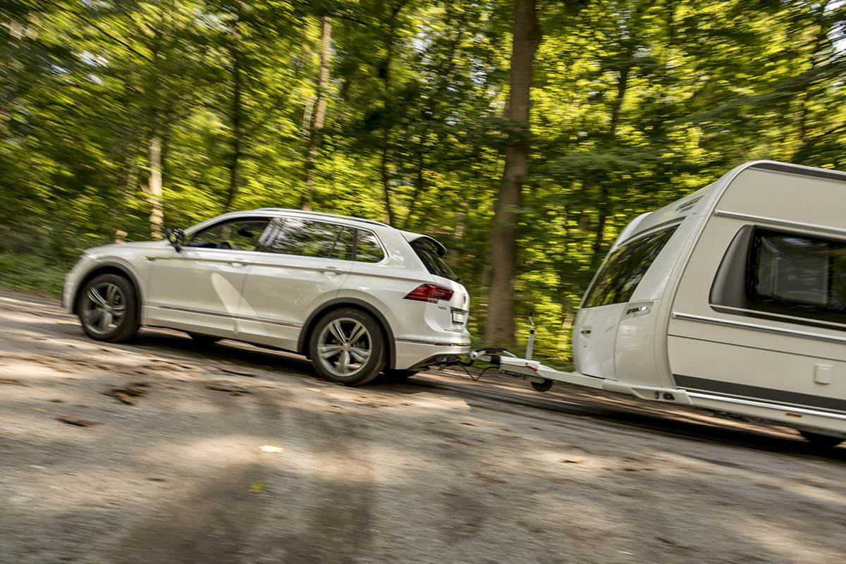 White Volkswagen Tiguan towing a caravan on a forest road with an ORIS AK41 vertically detachable towbar.