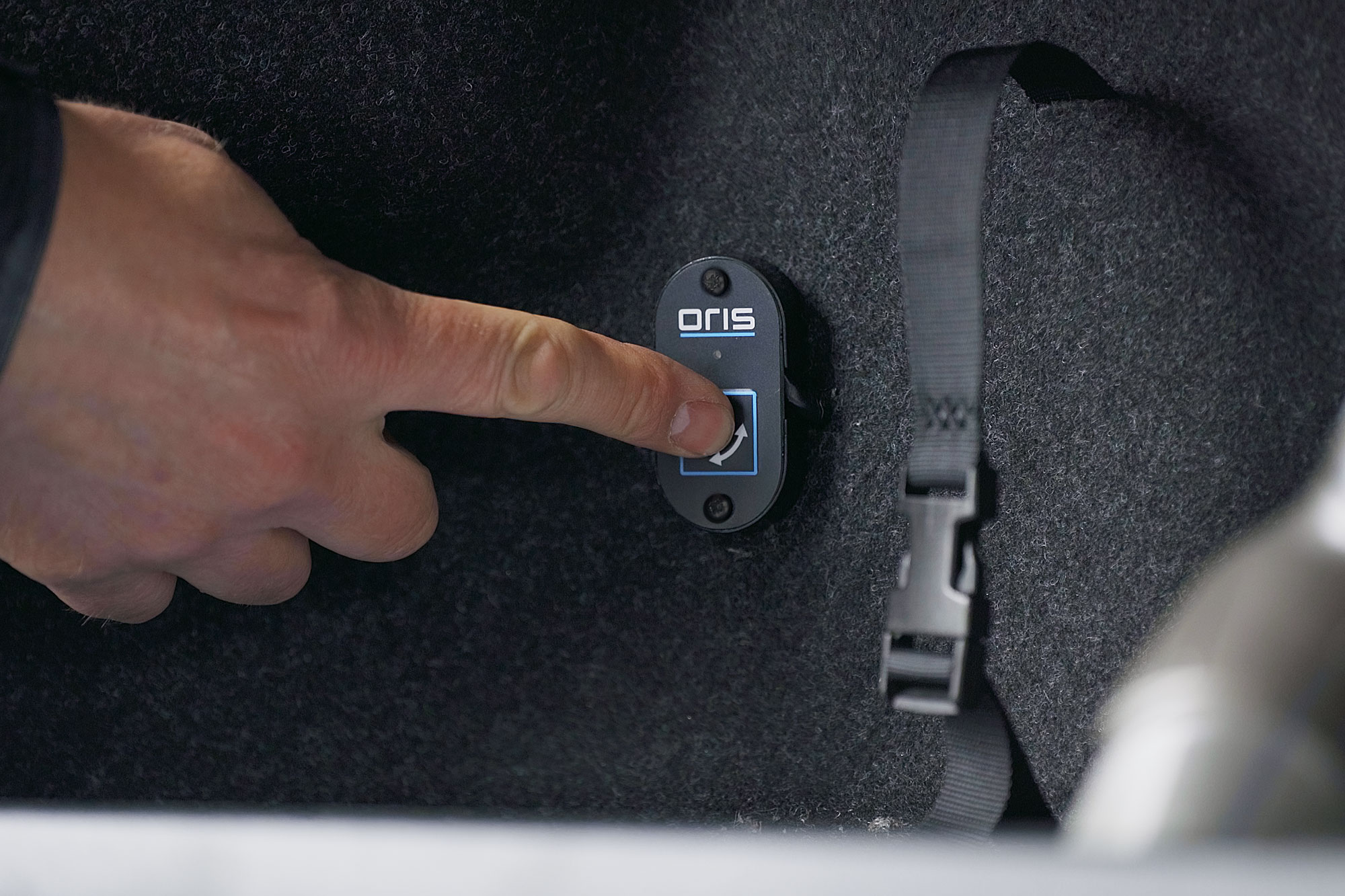 A thumb pressing the ORIS towbar release button inside a vehicle luggage compartment.