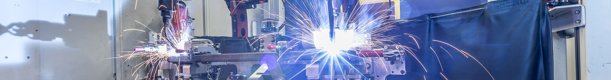 Automated welding robots manufacturing ORIS towbars and trailer hitch components with visible welding sparks in a production facility.