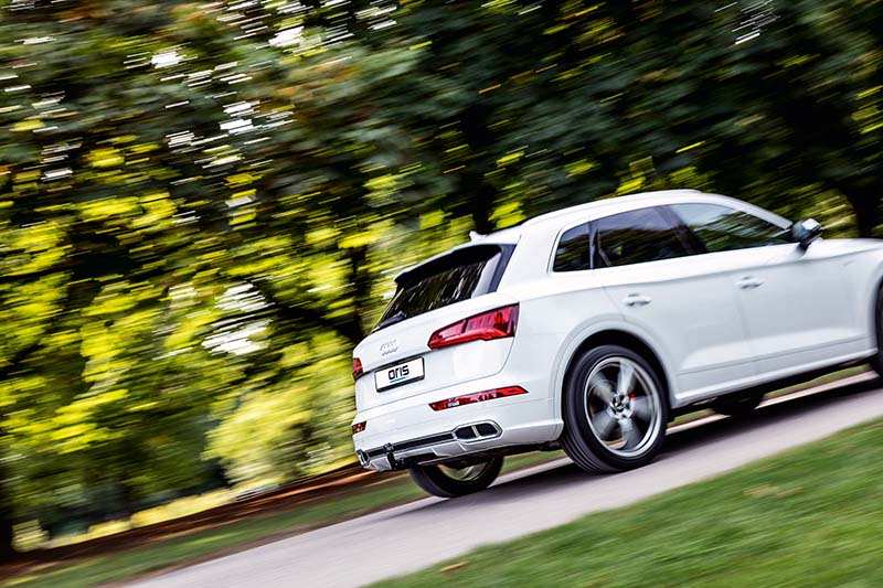 White Audi SUV driving on a tree-lined road with an ORIS towbar installed, surrounded by green woodland.