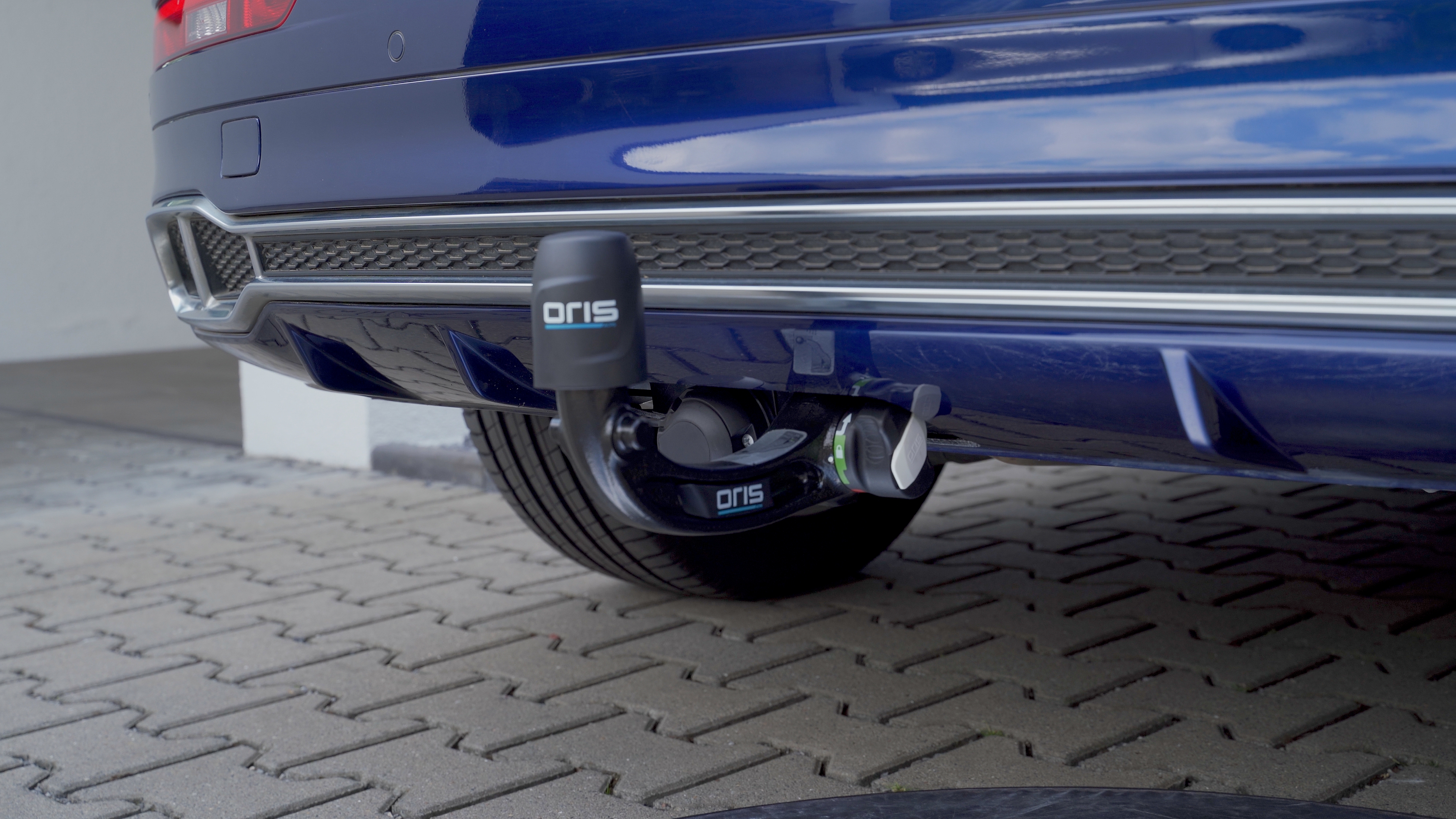 Close-up of an ORIS AK 4 FIX4BIKE® vertically detachable towbar with protective cap and electrical socket mounted on a blue vehicle.
