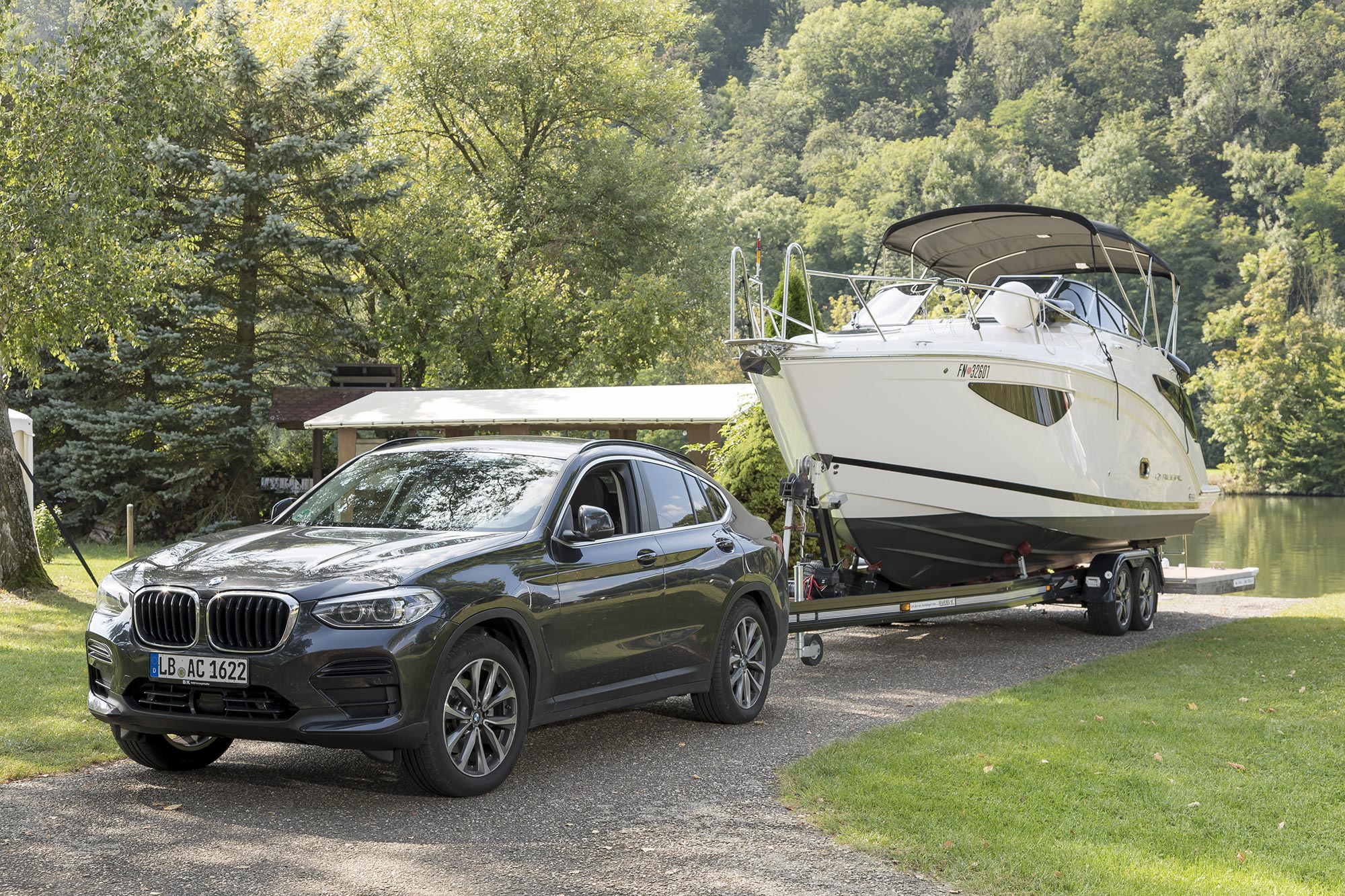 BMW X4 with ORIS FIX4BIKE® towbar towing a motorboat on a trailer near a waterside launch area.