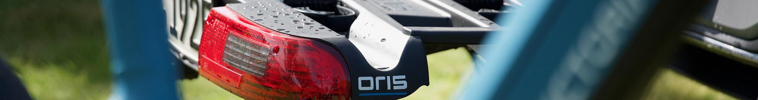 ORIS TRACC bicycle carrier close-up with integrated rear light, wheel rails and visible raindrops on the carrier surface for secure bike transport.