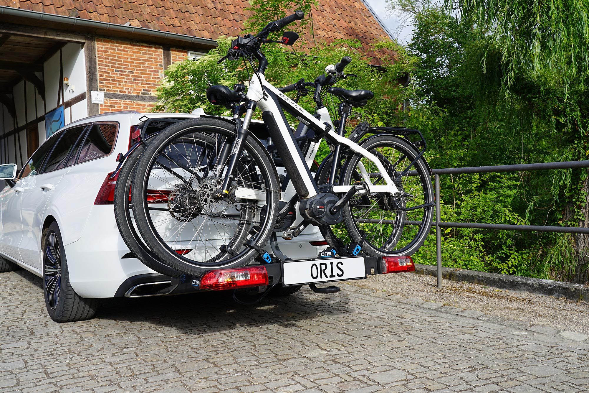 White Volvo estate car with the ORIS TRACC premium bike carrier transporting two e-bikes on the rear towbar.