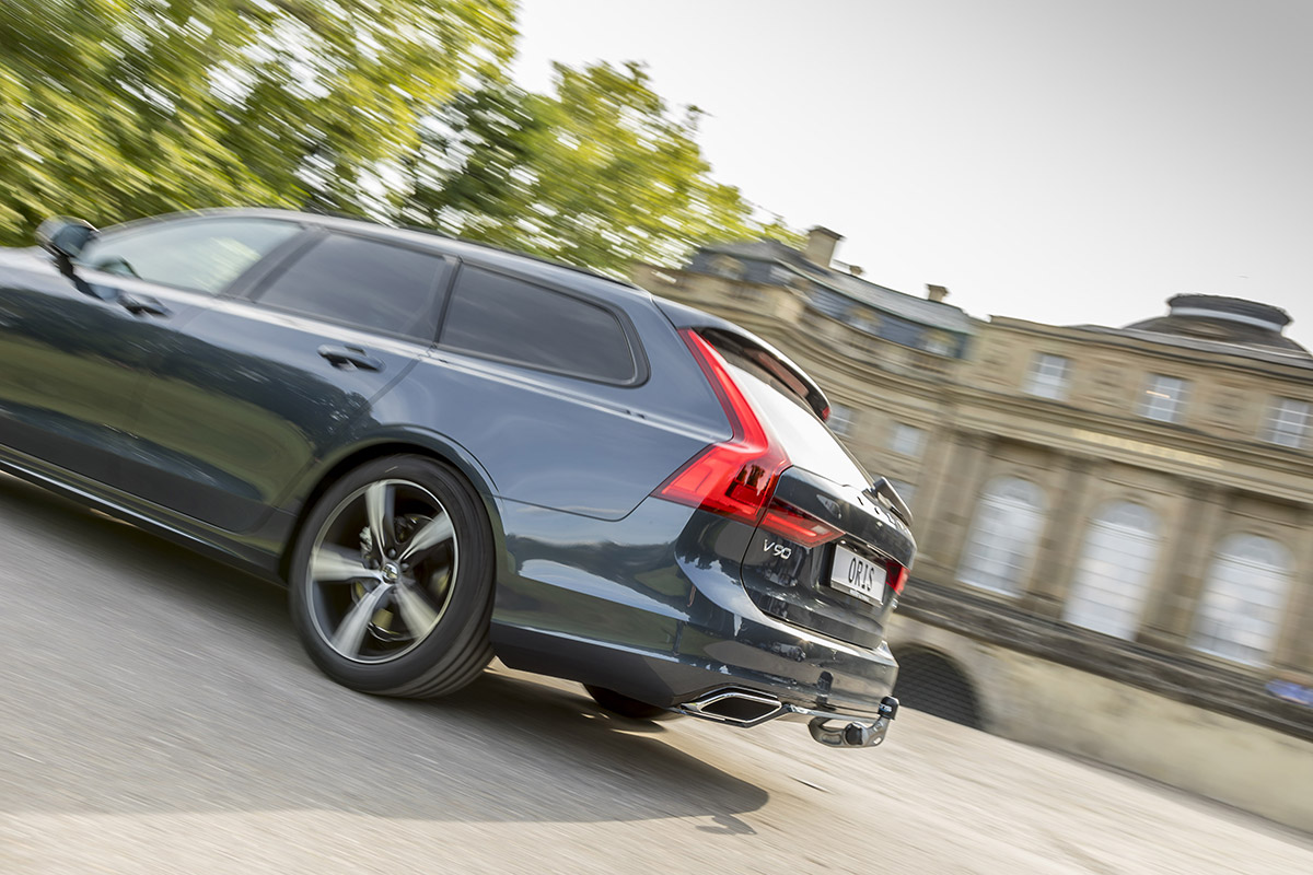 Volvo V90 estate driving on the road with an ORIS F4B detachable towbar installed, shown in a dynamic rear three-quarter view with motion blur.