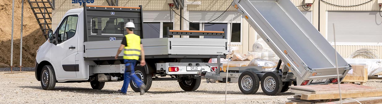 White flatbed truck with ORIS flanged towbar towing a tipper trailer at a construction site.