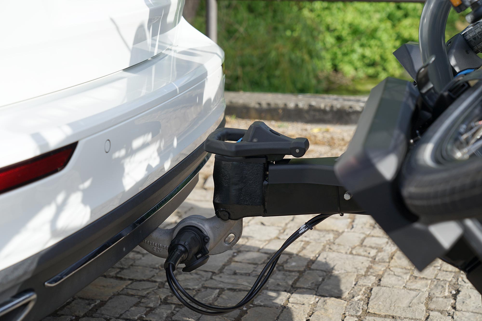 Close-up of a FIX4BIKE® towbar with an attached FIX4BIKE® bicycle carrier in the lowered position. A bicycle is mounted on the carrier, which is electrically connected to the vehicle via the towbar socket.