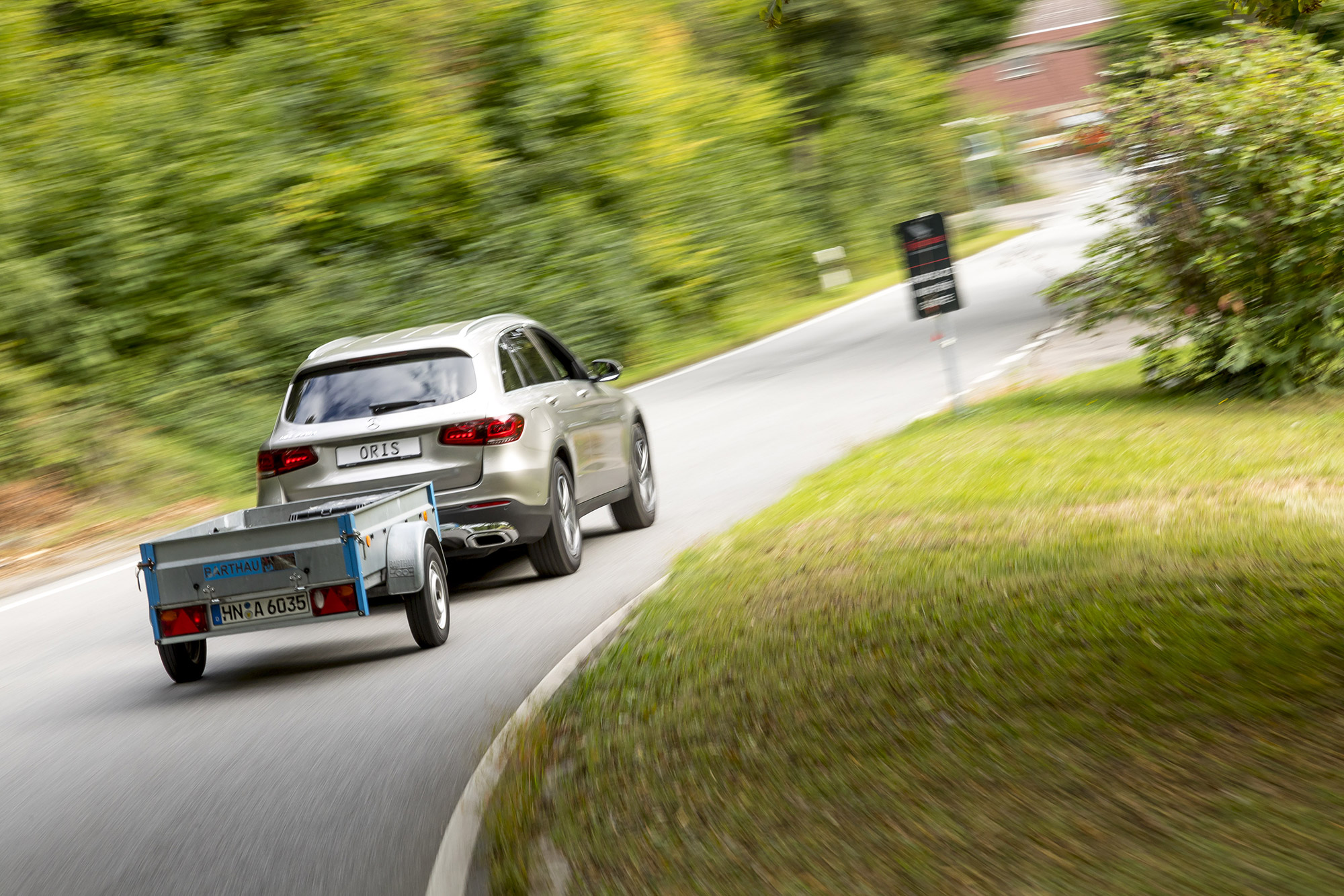 Silver Mercedes-Benz GLC towing a utility trailer with an ORIS AK4 detachable horizontal towbar on a country road.